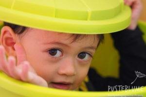 Ein kleiner Junge schaut aus einer Plastiktonne. 